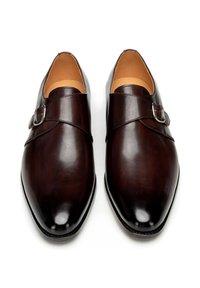 Paar glänzende dunkelbraune Leder-Monk-Strap-Herrenschuhe mit silbernen Schnallen, von oben auf weißem Hintergrund gesehen.