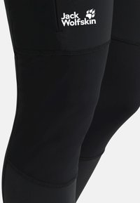 Leggings attivi neri realizzati in un tessuto morbido e elastico con un design cucito e logo Jack Wolfskin sulla coscia superiore.