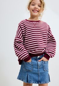 Sweter w paski w kolorze bordowym i jasnoróżowym z opuszczonymi ramionami, zestawiony z jasnoniebieską spódnicą dżinsową z dwoma przednimi kieszeniami i marszczonym dołem.