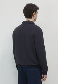 Giacca leggera blu navy realizzata in tessuto liscio, con colletto, orlo elastico e polsini con bottone. Vista posteriore mostrata.
