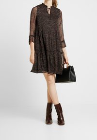 Svart klänning med färggård blommönster, semi-transparent tyg, lagerdesign, 3/4 ärmar, nyckelhålsringning, matchad med en svart handväska och bruna stövlar.