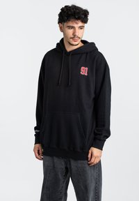 Schwarzer Kapuzenpullover mit einem roten "91"-Logo auf der Brust, Kordelzug-Kapuze, frontaler Kängurutasche und gerippten Bündchen. Weicher, strukturierter Stoff.