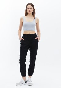 Svetle šedý žebrovaný crop top s širokými ramínky, spárovaný s černými joggingovými kalhotami s elastickým pasem a bočními kapsami. Nošeno s bílými teniskami.