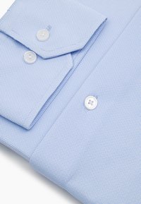 Jasnoniebieska koszula o strukturze delikatnej tkaniny, starannie złożona, z białymi guzikami na mankietach i listwie frontowej.