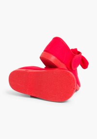 Czerwone buty z tkaniny o miękkiej fakturze, z solidną gumową podeszwą i zapięciem na rzep, ozdobione akcentem w postaci kokardy.