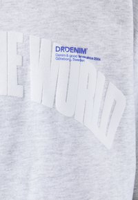 Sudadera gris con un gran texto blanco "EL MUNDO", y un pequeño logo azul de DRDENIM cerca de la parte inferior. Tela suave y texturizada.