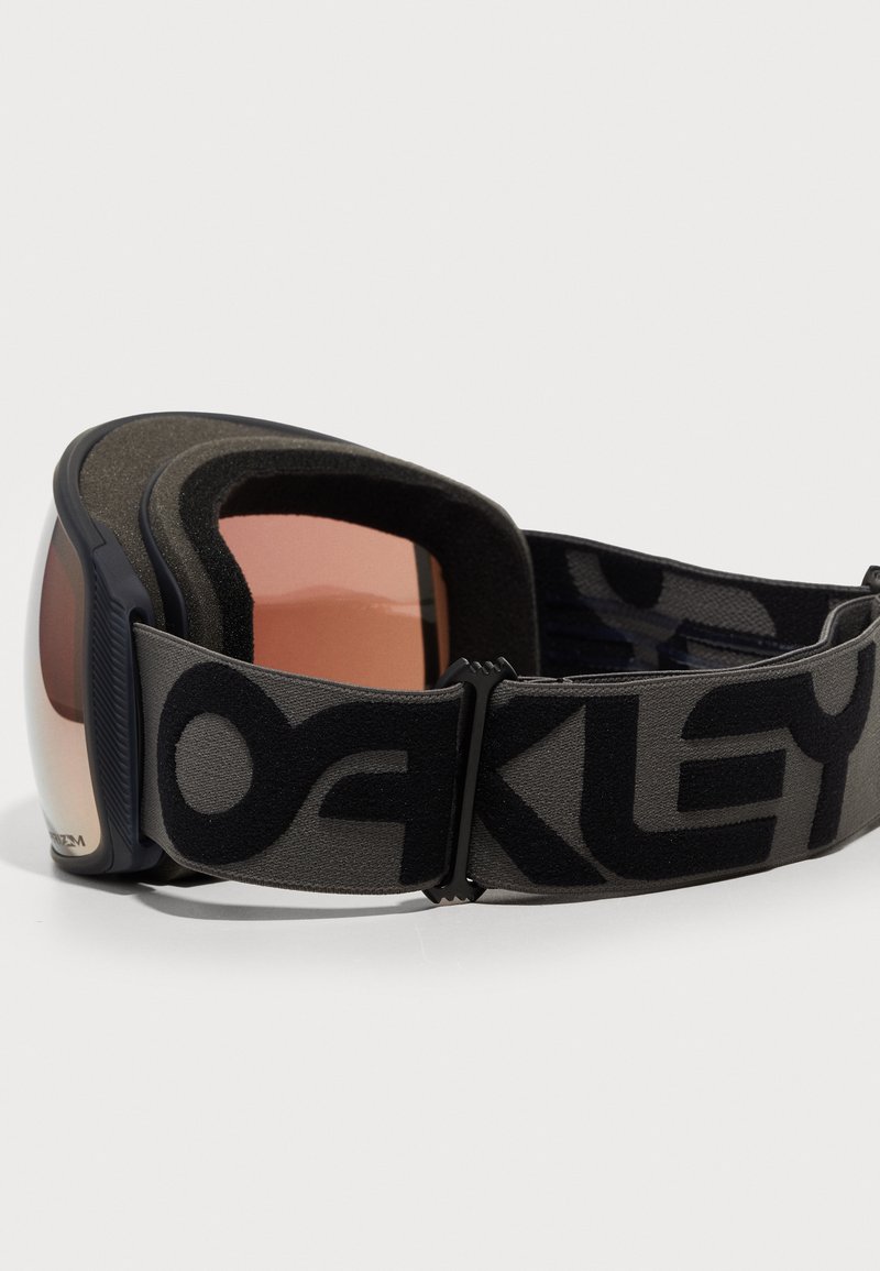 Black and gray ski goggles with a wide strap featuring the "Oakley" logo, tinted lenses, and a soft padded frame for comfort.