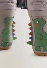 Detské nepremokavé čižmy v sivej farbe s prešívaným levanduľovým zvrškom. Obsahujú zelené akcenty dinosaura na oboch stranách a textúrované gumové podrážky.