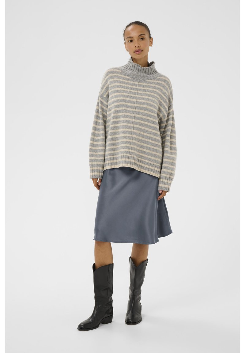 Pull tricot rayé gris et crème avec un col montant, associé à une jupe satin bleu ardoise longueur genoux et des bottes noires jusqu'aux genoux.