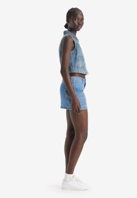 Set di giubbotto in denim e pantaloncini in azzurro chiaro, design corto con colletto rotondo, tasca frontale e orlo sfilacciato, abbinato a sneakers bianche.
