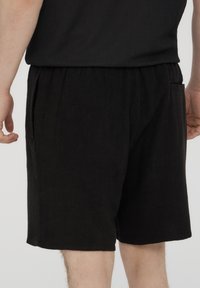 Pantaloni corti neri realizzati in materiale testurizzato, con una fascia elastica in vita e tasche laterali, mostrati dal retro con un fit rilassato.