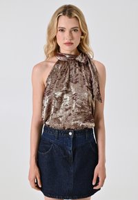Top a halter in bronzo lucido con dettaglio fiocco, abbinato a una mini gonna in denim scuro con tasche frontali e chiusura con bottone.