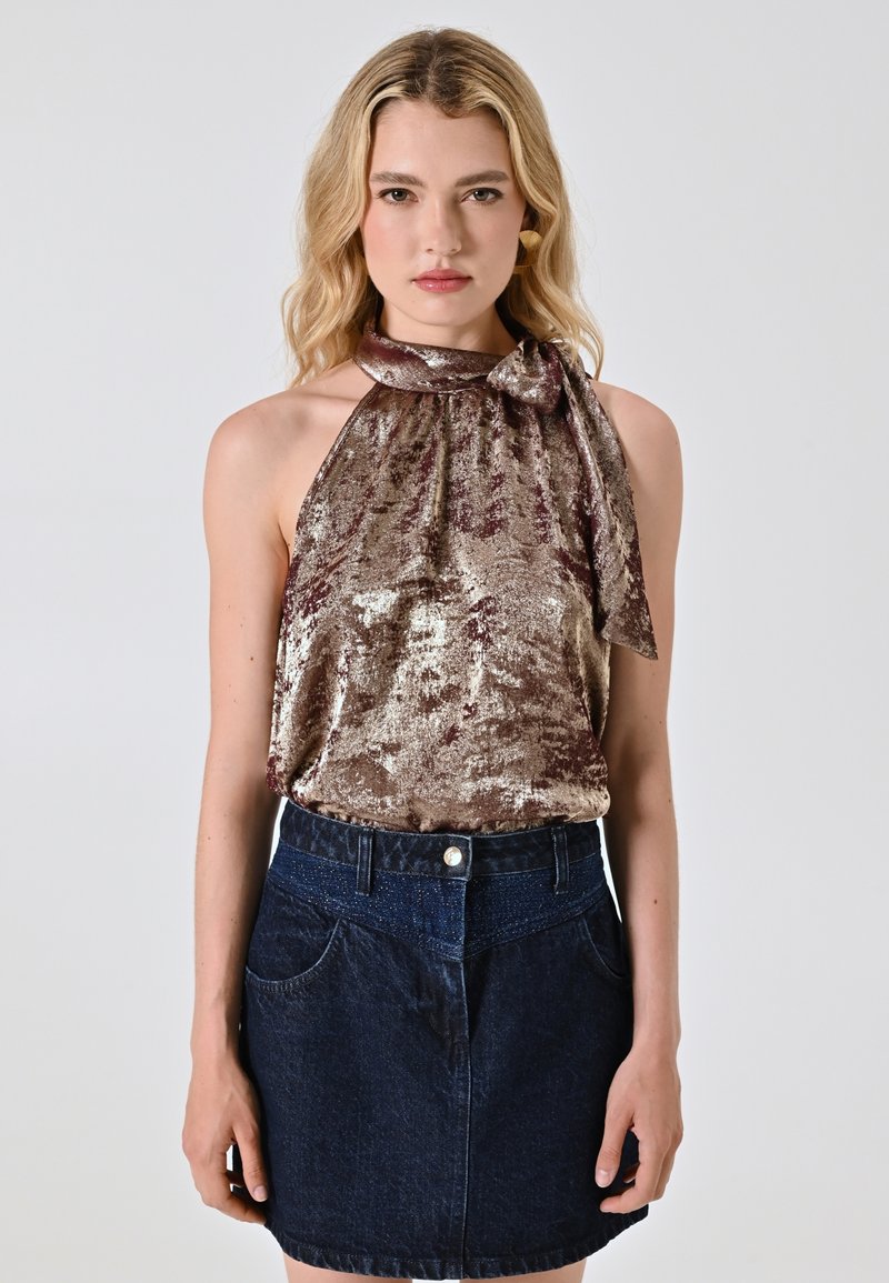 Top a halter in bronzo lucido con dettaglio fiocco, abbinato a una mini gonna in denim scuro con tasche frontali e chiusura con bottone.