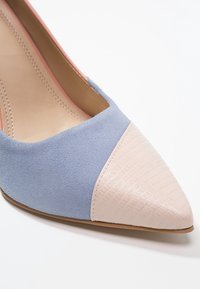 Pumps med spetsig tå som har en blå mockaskinnovansidan och en texturerad beige lackläder tåkappa. Inkluderar en rosa innerfoder och en smal klack.