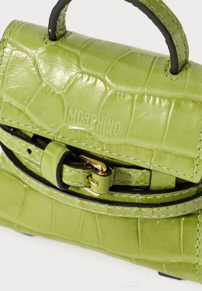 Pequena bolsa de couro verde com relevo de crocodilo, com alça superior, fivela dourada e logótipo Moschino Milano em relevo no flap frontal.