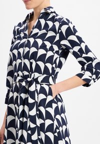 Navy-Kleid mit weißem Halbmondmuster, mit Kragen, Knopfverschluss vorne, tailliertem Bund und 3/4-Ärmeln. Aus glattem Stoff gefertigt.