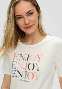 Witte katoenen t-shirt met meerkleurige "ENJOY" tekst in verschillende lettertypen en stijlen, met een ronde halslijn en korte mouwen.