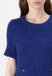 Blauwe textuur jurk met korte mouwen, voorzien van een rasterpatroon, franjes bij de hals en een zilveren hardware accent op de taille.