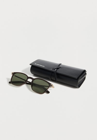 Γυαλιά ηλίου με μαύρο σκελετό και πράσινους φακούς τοποθετημένα δίπλα σε ένα ρολοποιημένο μαύρο δερμάτινο θήκη Montblanc πάνω σε λευκή επιφάνεια.