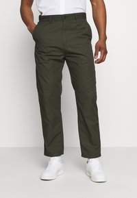 Groene, lichte broek met een recht model, voorzakken en een knoopsluiting, gecombineerd met witte sneakers.