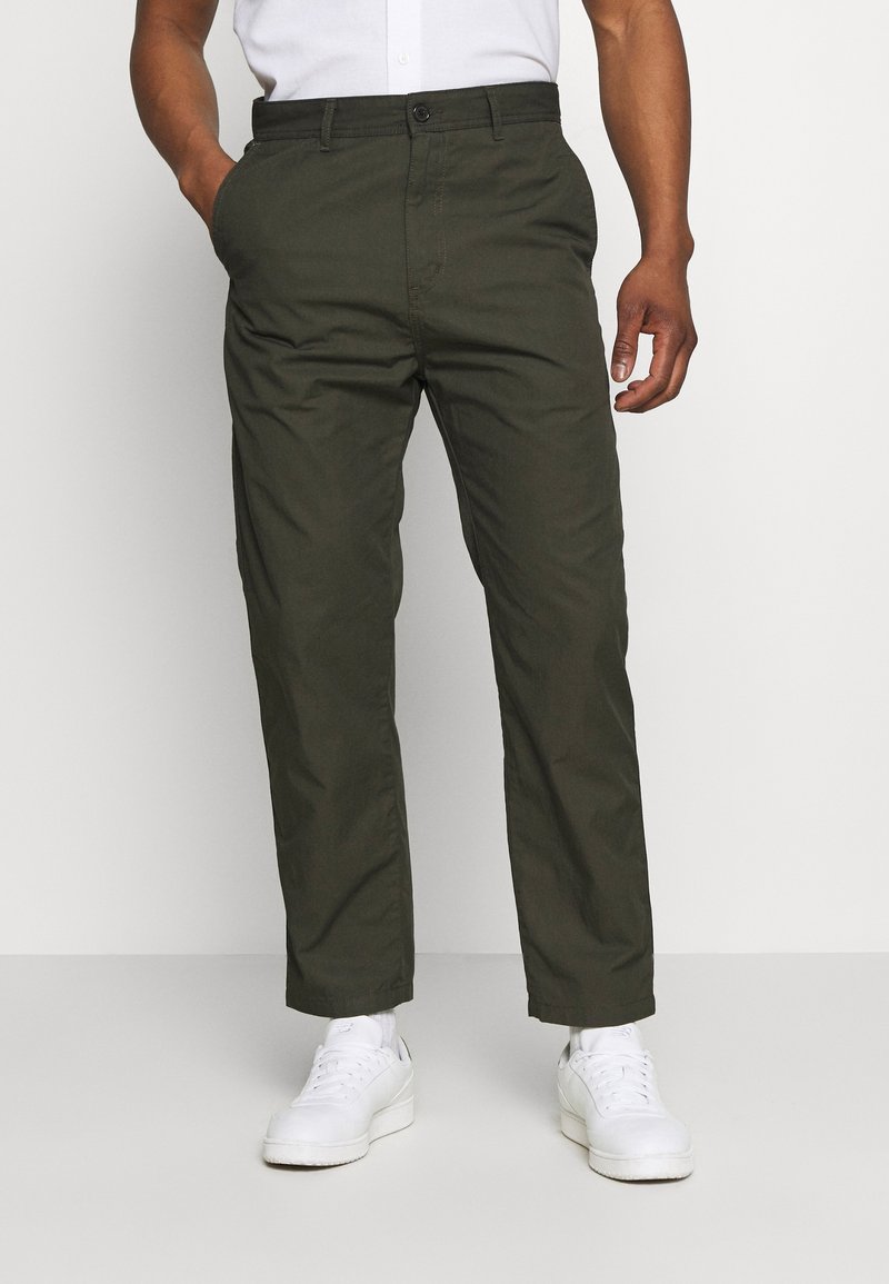 Groene, lichte broek met een recht model, voorzakken en een knoopsluiting, gecombineerd met witte sneakers.