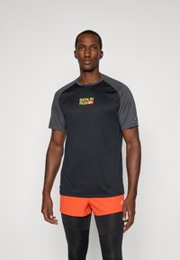 Sort trænings T-shirt med grå raglanærmer, der har "BERLIN RUN" i gul og rød print på brystet. Letvægts, fugttransporterende materiale.