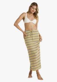 Gestreepte maxi rok in geel, bruin en wit; gebreide textuur met een striktaille en een rechte silhouet. Gekozen voor een crème bralette.