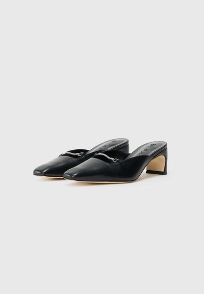 Mule in pelle nera con punta affusolata, tacco basso e decorazioni in metallo argentato sulla parte frontale. Texture liscia e design elegante.