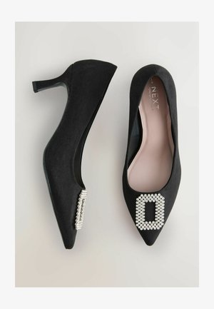 Mustadest sametist kõrge kontsaga kingad, millel on terav nina ja dekoratiivne rhinestone pannal igas sõrmes. Sile sisemine vooder; kitsas konts.