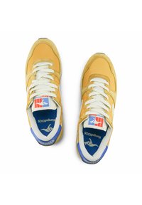 Sneaker gialli con lacci bianchi e un accento blu. Presentano una suola in gomma e una parte superiore in tessuto, con dettagli del logo sulla linguetta e sul tallone.