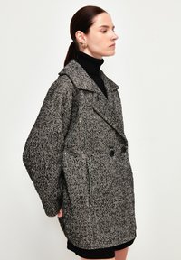 Cappotto a righe a spina di pesce bianco e nero con davanti doppiopetto, ampio colletto e maniche over. Presenta due tasche frontali.