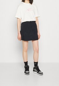 Svart, strukturerad kjol med dragsko i midjan, kombinerad med en vit Nike-t-shirt med en ljusrosa logotyp, svarta strumpor och högstövlade sneakers.