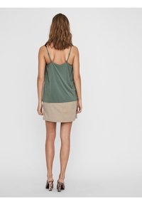 Top senza maniche di colore verde oliva con spalline sottili, abbinato a una mini gonna color sabbia. Tessuto testurizzato con una finitura liscia e una vestibilità casual.