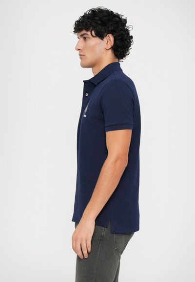 Pólo azul marinho com colarinho clássico, mangas curtas, fendas laterais e um logótipo discreto no peito. Feito em tecido suave e respirável.