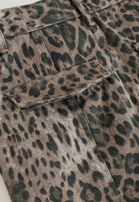 Leopardi mustriga denim kangas, millel on tumedad rohelised laigud heles pruuni taustal, nähtava õmbluse ja tagatasku detailiga.