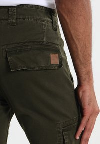 Pantalones cargo verde olivo hechos de tela resistente, con bolsillos laterales, un bolsillo trasero con una etiqueta de cuero y un corte relajado.