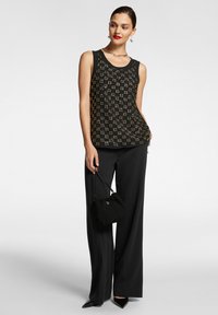 Blusa nera senza maniche con tessuto a fantasia e dettagli dorati, abbinata a pantaloni neri a vita alta e una piccola borsa nera.