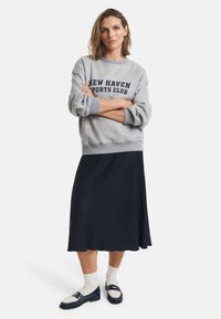 Gray sweatshirt with "NEW HAVEN SPORTS CLUB" in navy, paired with a black A-line skirt. Worn with white socks and navy shoes.