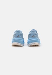 Baskets de sport bleu clair avec une tige en mesh, un col rembourré et une semelle extérieure en caoutchouc blanche. Présente un logo argenté à trois rayures au niveau du talon.