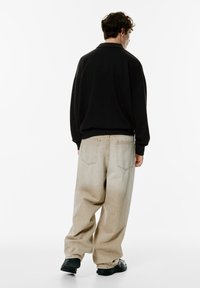Schwarzer, langärmeliger Pullover mit Kragen, kombiniert mit lockeren, hellbeigen Jeans mit Gesäßtaschen. getragen mit schwarzen Turnschuhen.