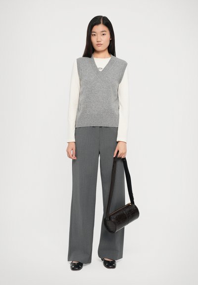 Grey knitted vest with v-neck, worn over a cream long-sleeve top. Paired with grey wide-leg trousers and a brown crossbody bag.