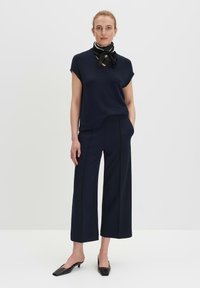 Maglietta blu navy a maniche corte con scollo a V e spacchi laterali, abbinata a pantaloni navy a gamba larga. Gli accessori includono una sciarpa bianco e nera e mule nere.