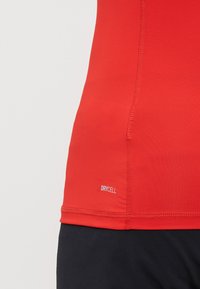Rød atletisk tanktopp laget av fukttransporterende stoff. Har flatlock-sømmer og "DRYCELL"-merke i kanten. Slank og tettsittende design.