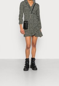 Green wrap dress with black leopard print, long sleeves, ruffled collar, paired with black chunky-heeled boots and a small black crossbody bag.