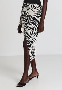 Schwarz-weißer Zebra-Print-Midirock mit seitlichem Schlitz und silbernen Beschlägen, aus leichtem Stoff gefertigt.