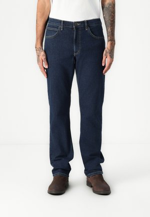 Mørkeblå denim jeans med rett passform, som har fem lommer og kontraststing. Brukes med brune lærstøvler.