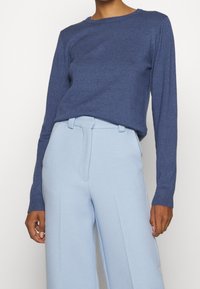 Námořnický modrý svetr s dlouhým rukávem z měkkého pleteného materiálu, spárovaný se světle modrými kalhotami s vysokým pasem a hladkou texturou.