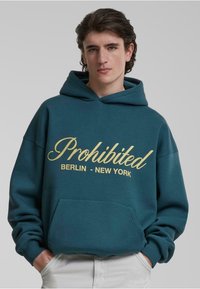 Teal hættetrøje lavet af blød stof, med en frontlomme og tekst i skriftskrift "Forbudt BERLIN - NEW YORK" i gul. Justerbar snøre hætte.