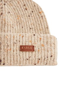 Bēša adīta cepure ar ribotu tekstūru, kurai ir oranži un brūni punkti. Iekļauta brūna ādas birka ar iepresēto tekstu "FABLE ENGLAND".