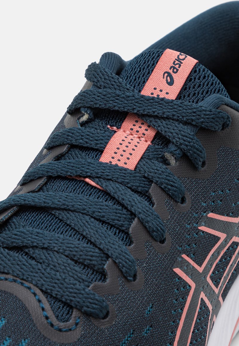 Baskets sportives avec une tige en maille bleu foncé, des accents rose clair, des lacets texturés et une semelle rembourrée au design ondulé.